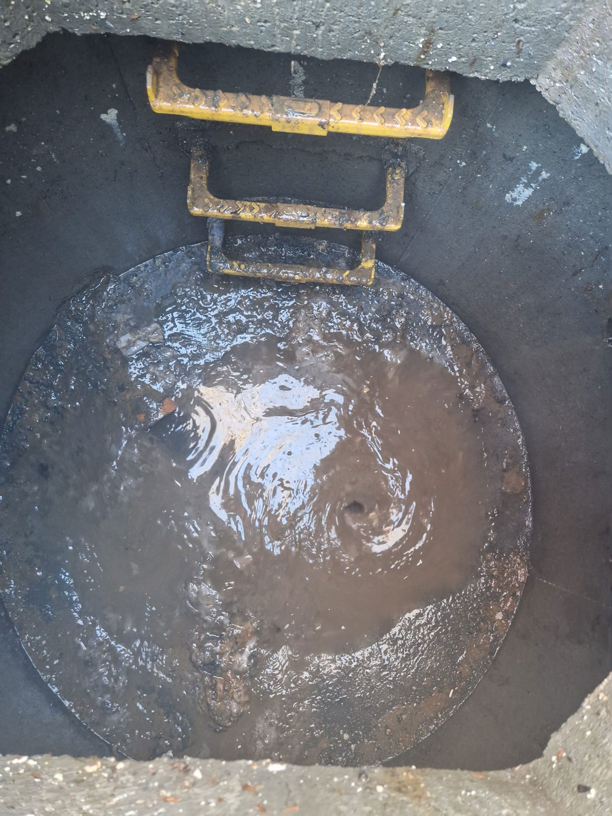 Declan from Drain Ace clearing a blocked drain in Esher with water forming a whirlpool in a deep manhole after the blockage was removed