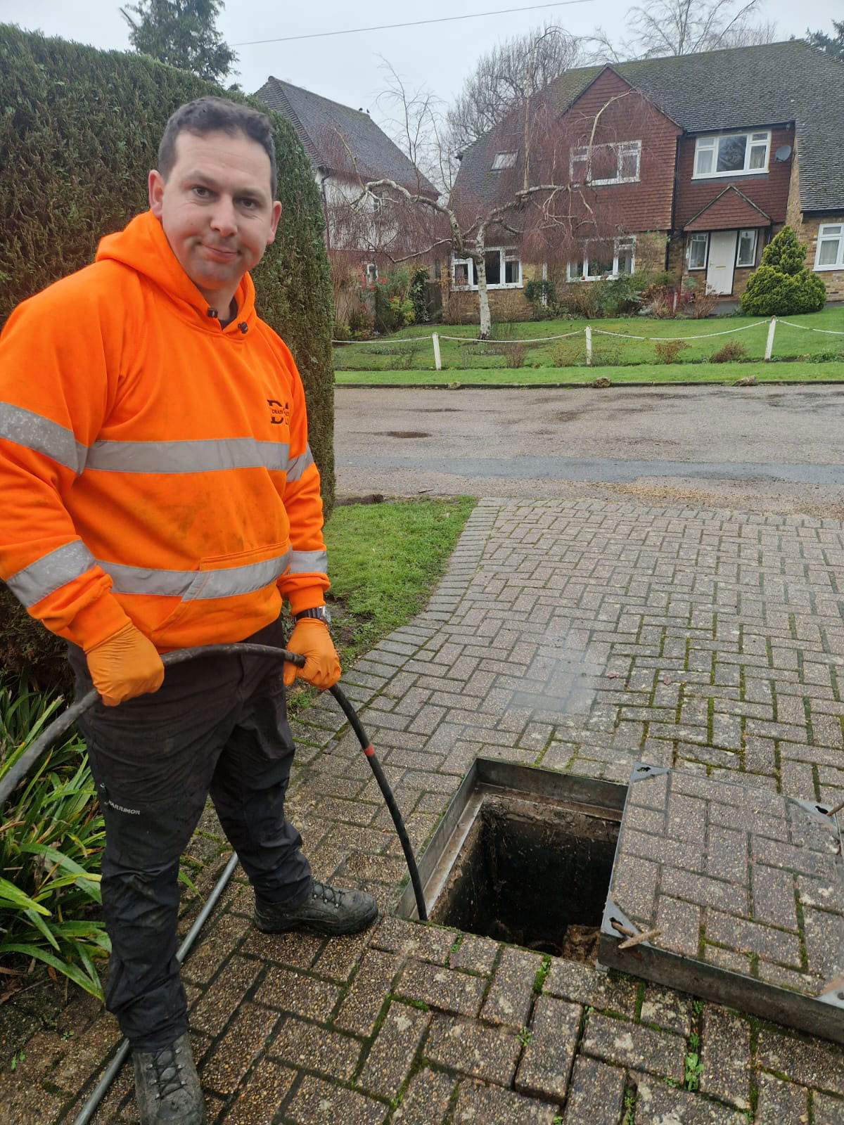Drain jetting to clear blocked drain in Weybridge Declan from Drain Ace jet washing a blocked drain in Weybridge with the manhole cover lifted on a brick driveway